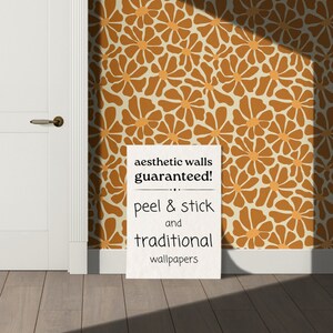 Może przedstawiać: Biały znak z czarnym tekstem, kt&oacute;ry brzmi "aesthetic walls guaranteed! ... peel & stick and traditional wallpapers" na tle brązowo-pomarańczowej tapety z kwiatowym wzorem.