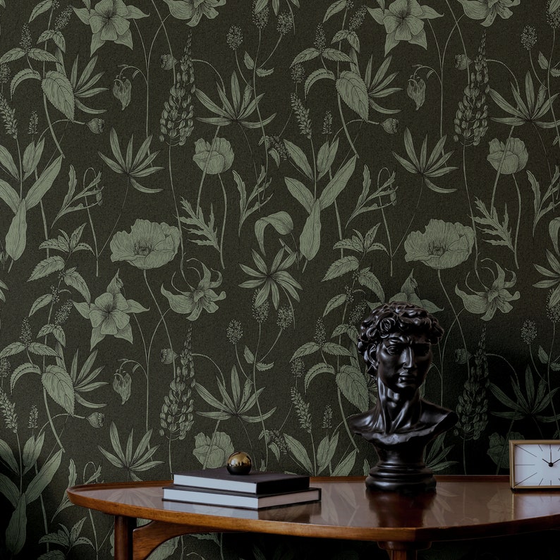 May include: A dark green wallpaper featuring a botanical pattern of leaves and flowers. A black bust of a man and two books are on a wooden table in front of the wallpaper.