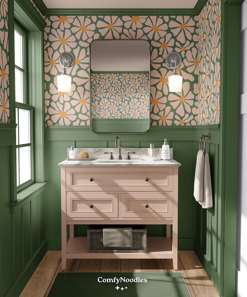K&ouml;nnte beinhalten: Ein rosa Badezimmer-Waschtisch mit drei Schubladen und einem unteren Regal. Der Waschtisch steht vor einer gr&uuml;nen Wand mit einem floralen Tapetenmuster. Die Tapete zeigt rosa und orangefarbene Blumen auf gr&uuml;nem Hintergrund. Ein Spiegel h&auml;ngt &uuml;ber dem Waschtisch.