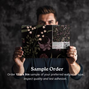May include: A person is holding a sample order of wallpaper. The wallpaper is a dark floral pattern with pink and green flowers on a black background. The sample is 13 inches by 9 inches. The text on the sample reads "Sample Order" and "Order 13in x 9in sample of your preferred wallpaper type. Inspect quality and test adhesion."
