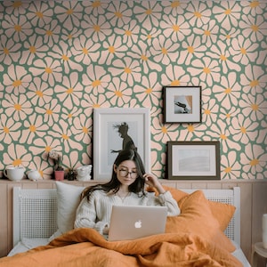 K&ouml;nnte beinhalten: Eine Frau sitzt im Bett mit einem Laptop und arbeitet oder surft im Internet. Das Bett hat ein wei&szlig;es Kopfteil und eine gr&uuml;n-rosa gemusterte Tapete mit Blumen. Hinter der Frau h&auml;ngen zwei gerahmte Bilder an der Wand.