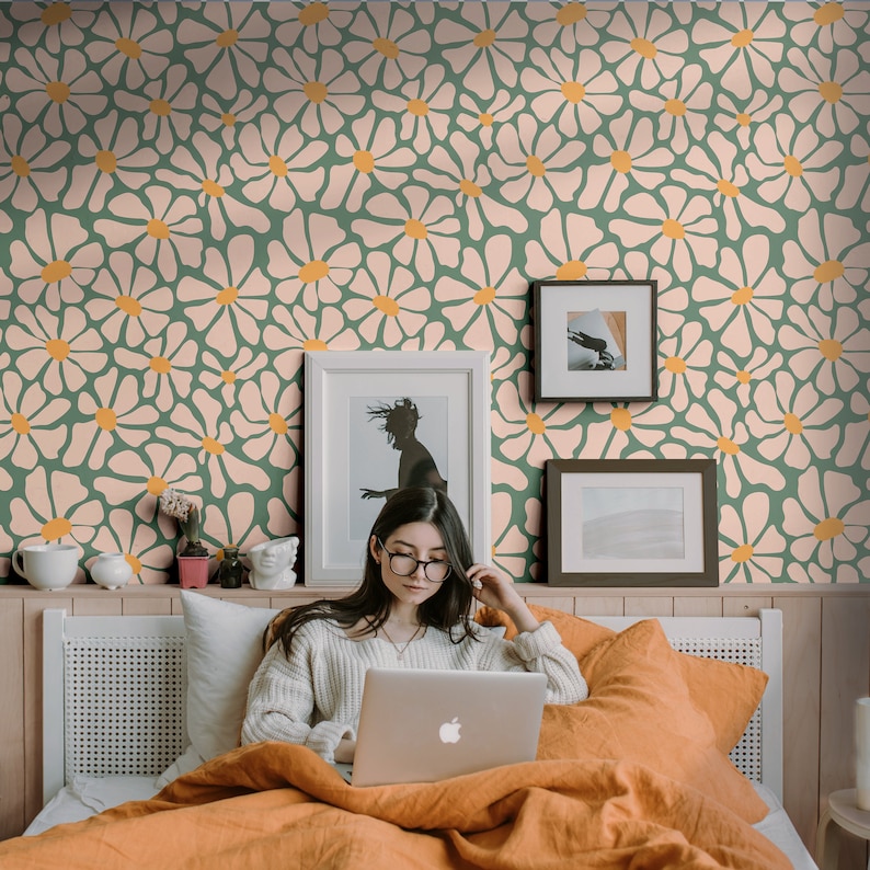 K&ouml;nnte beinhalten: Eine Frau sitzt im Bett mit einem Laptop und arbeitet oder surft im Internet. Das Bett hat ein wei&szlig;es Kopfteil und eine gr&uuml;n-rosa gemusterte Tapete mit Blumen. Hinter der Frau h&auml;ngen zwei gerahmte Bilder an der Wand.
