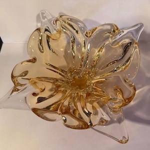 May include: A decorative glass bowl in the shape of a flower. The bowl has a clear, petal-like design with amber and clear glass. The center of the bowl is a darker amber color, and the petals are a lighter amber.