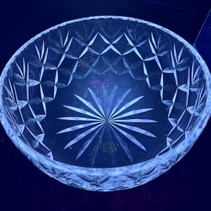 Puede incluir: Un cuenco redondo de cristal transparente con un diseño de estrella en el centro y patrones en forma de diamante alrededor del borde. El cuenco está hecho de cristal tallado y refleja la luz, creando un efecto brillante. El cuenco se utiliza probablemente para servir o exhibir.