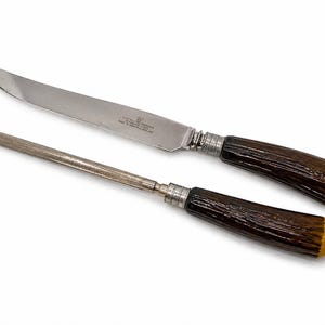 Peut inclure: Un ensemble de couteau à découper et d'acier à aiguiser. Le couteau a une lame incurvée et un manche marron foncé avec des accents argentés. L'acier à aiguiser a une poignée similaire. Les extrémités des poignées sont jaunes.