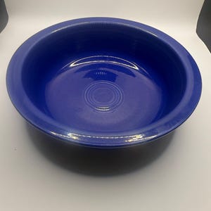 May include: A cobalt blue ceramic bowl with a wide rim. The bowl has a circular shape and a glossy finish. The interior of the bowl has a concentric circle design in the center. This bowl is suitable for serving food.