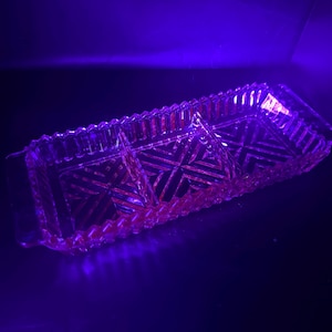 Könnte beinhalten: Ein rechteckiges Serviertablett aus klarem Glas mit drei Fächern. Das Tablett hat ein strukturiertes, geometrisches Muster und einen gewellten Rand. Das Bild ist mit einem violetten Farbton beleuchtet.