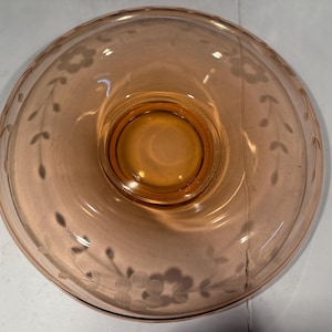 Könnte beinhalten: Eine klare, pfirsichfarbene Glasschale mit einem zentralen, erhöhten Sockel. Der Rand der Schale ist mit geätzten Blumen- und Blattmustern verziert. Die Schale ist wahrscheinlich vintage und eignet sich zum Servieren oder Ausstellen.