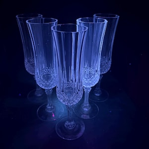 Peut inclure: Cinq flûtes à champagne en cristal transparent avec un motif taillé en diamant sur la partie inférieure du verre. Les flûtes ont un design long et élancé et sont disposées sur une surface sombre, créant une esthétique sophistiquée.