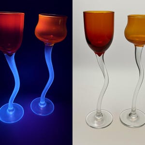 May include: Two sets of unique wine glasses. The glasses have a clear, curved stem and a colored bowl. One set has a red bowl and a blue stem, while the other has an orange bowl and a clear stem. The glasses are on a white background.