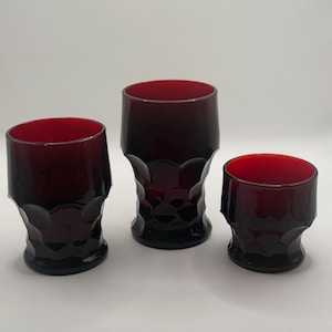 Peut inclure: Trois verres à boire rouge rubis avec un motif géométrique. Les verres sont de tailles différentes, avec une large ouverture et un corps texturé et facetté. Les verres sont probablement vintage et sont posés sur un fond blanc uni.