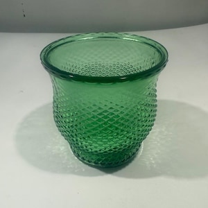 Könnte beinhalten: Ein grüner Glas-Kerzenhalter mit Rautenmuster. Der Kerzenhalter hat eine breite, offene Oberseite und einen leicht ausgestellten Boden. Das Glas hat einen leuchtenden Grünton, und das Rautenmuster verleiht der Oberfläche Textur.