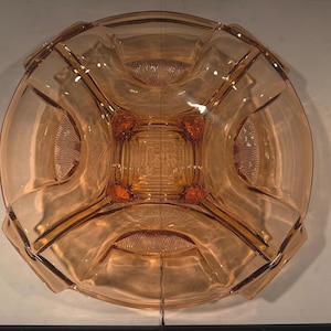 Könnte beinhalten: Eine Vintage-Servierschale aus pfirsichfarbenem Glas. Die Schale hat eine kreisförmige Form mit einem quadratischen Mittelteil und vier gebogenen Abschnitten. Jeder Abschnitt hat ein strukturiertes, fächerartiges Design. Der Rand hat ein geometrisches Design.