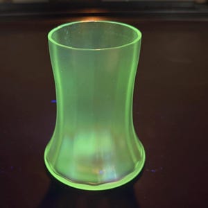 Peut inclure: Un vase en verre vert avec une base évasée et un sommet cylindrique. Le vase a une forme lisse et incurvée et une apparence translucide. Le verre a une légère lueur.