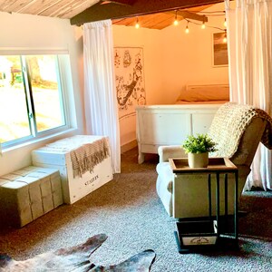 Puede incluir: Vista interior de una habitaci&oacute;n con techo de madera y alfombra de piel de vaca. Incluye un sill&oacute;n blanco, una mesa auxiliar con una planta y un arc&oacute;n blanco con la palabra "STARLES" impresa.