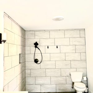 Puede incluir: Un ba&ntilde;o moderno con una ducha a ras de suelo con paredes de azulejos grises claros y un cabezal de ducha negro. Un inodoro blanco y un suelo de hormig&oacute;n gris oscuro completan el espacio. La habitaci&oacute;n est&aacute; bien iluminada.