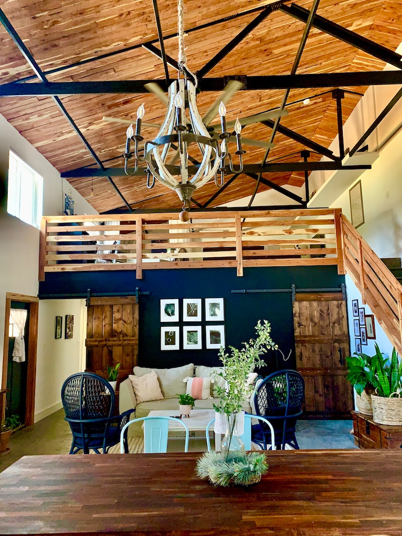 Puede incluir: Vista interior de una sala de estar con un techo alto de madera y una gran l&aacute;mpara de ara&ntilde;a. La habitaci&oacute;n cuenta con un &aacute;rea de loft, un sof&aacute; y dos sillas azules. Una mesa de madera oscura est&aacute; en primer plano.