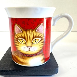 May include: A ceramic mug featuring a detailed illustration of a tabby cat with yellow eyes and a red collar. The mug has a white handle and rim, with a red background adorned with floral patterns. The mug is approximately 4 inches tall.