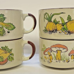 May include: Four cream-colored ceramic mugs with brown handles and rims. Each mug features a different vegetable illustration: celery, lemons, onions, and mushrooms. The mugs are stacked in pairs.