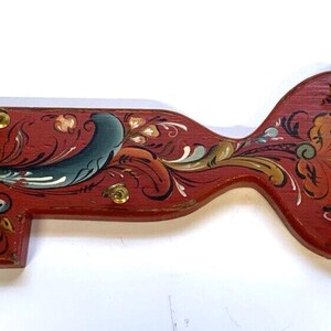 May include: A red wooden key-shaped wall hook with hand-painted floral designs in shades of red, gold, blue, and green. The hook is a traditional Scandinavian folk art design.