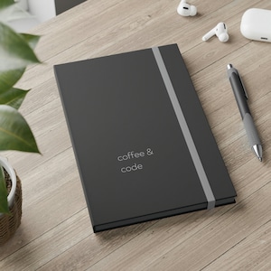 May include: A black notebook with a gray elastic band closure. The notebook has the text "coffee & code" printed in white on the front cover.