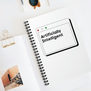 May include: A white spiral bound notebook with a black and white illustration of a computer window. The window has the text "Artificially Intelligent" inside.