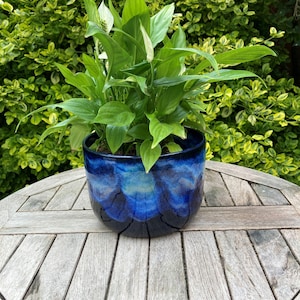 Puede incluir: Una planta de lirio de la paz de color verde vibrante con espatas blancas en una maceta redonda de cerámica esmaltada. La maceta presenta un acabado brillante profundo que transita de un azul marino oscuro en la base a un azul cobalto moteado.