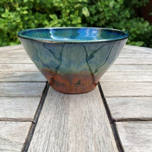 May include: A ceramic bowl featuring a smooth, rounded shape with a glossy glaze. The interior and upper exterior are a deep, vibrant blue, transitioning into a muted teal midsection, and finishing with a textured, earthy reddish-brown base.