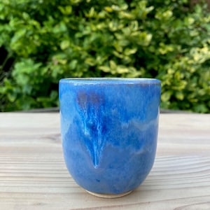May include: A blue ceramic mug with a white glaze. The mug has a unique, marbled pattern.