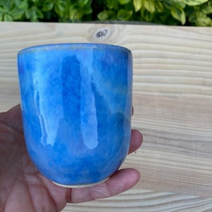 Puede incluir: Una taza pequeña de cerámica azul con un esmalte blanco. La taza tiene un aspecto moteado y marmoleado.