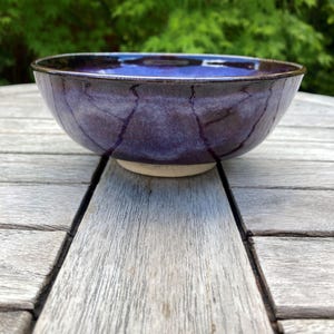 Peut inclure: Un bol en céramique présentant un émail bleu et violet profond avec des motifs de veines sombres semblables à des craquelures sur tout l'extérieur. Le bol possède un bord arrondi lisse et une base circulaire claire non émaillée.
