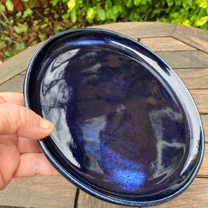 Könnte beinhalten: Ovalförmige, dunkelblaue Keramikservierplatte mit glänzendem Finish. Die Platte hat einen leicht erhöhten Rand und eine tiefe, satte Farbe mit subtilen Variationen. Die handgefertigte Keramik eignet sich zum Servieren von Vorspeisen oder kleinen Gerichten.