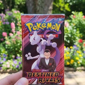 May include: A red and purple Pokémon trading card pack with the Pokémon logo and the text "Destined Rivals". The pack features an illustration of Mewtwo and a man in a suit. The pack contains 10 additional game cards.