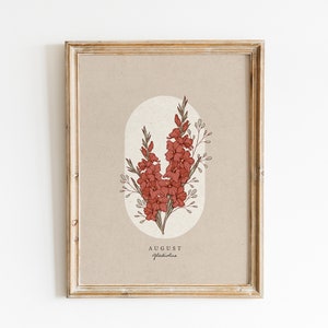 May include: A framed print with a beige background featuring a botanical illustration of a red gladiolus flower with the text "AUGUST Gladiolus" at the bottom.