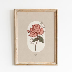 May include: A framed print with a beige background featuring a pink rose with green leaves and stems. The rose is surrounded by a light beige oval. The text "JUNE" and "Rose" is printed below the rose.