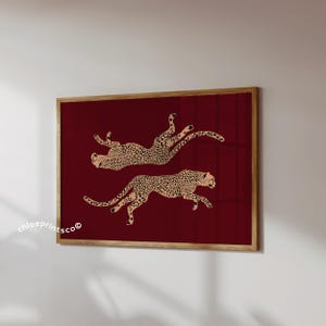 May include: A framed art print featuring two cheetahs in a running pose against a deep red background. The cheetahs are tan with black spots. The print is in a wooden frame. The text "chloeprints.co" is in the lower left corner.