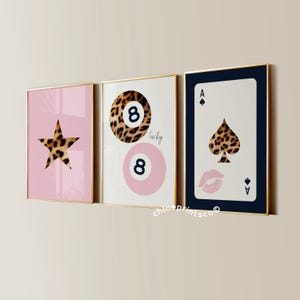 Peut inclure: Trois impressions d'art encadrées avec une bordure dorée. Les impressions présentent une étoile, un motif de boule de billard porte-bonheur et un as de pique, tous avec un motif léopard. Les couleurs de fond sont rose, blanc et bleu marine.