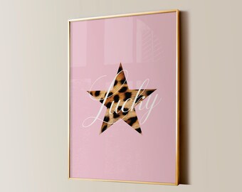 May include: A pink framed print with a gold frame. The print features a large white star with a leopard print pattern inside. The word "Lucky" is written in white cursive script inside the star.