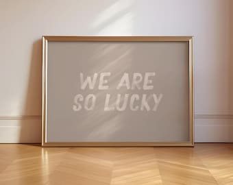 May include: A gold framed picture with a light gray background and the text "We are so lucky" in white.