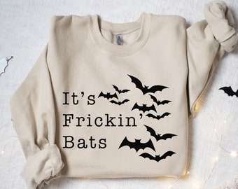 May include: Sand-colored sweatshirt with the phrase "It's Frickin' Bats" and a flock of black bat silhouettes. The design is centered on the front of the long-sleeved top, perfect for Halloween or spooky season.