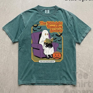 May include: A blue spruce t-shirt featuring a graphic of a ghost reading a book in a purple armchair with a black cat and a jack-o'-lantern. The text reads The Midnight Readers Society and JUST ONE MORE CHAPTER, surrounded by flying bats.