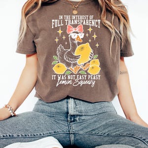 Peut inclure: T-shirt marron avec un dessin d'oie portant des lunettes de soleil et un n&oelig;ud, tenant un citron. Le texte dit "IN THE INTEREST OF FULL TRANSPARENCY" et "IT WAS NOT EASY PEASY Lemon Squeezy".