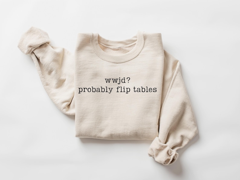 Peut inclure: Un sweat-shirt cr&egrave;me avec le texte "wwjd? probably flip tables" en noir. Les manches longues sont retrouss&eacute;es. Le sweat-shirt est fait d'une mati&egrave;re douce.