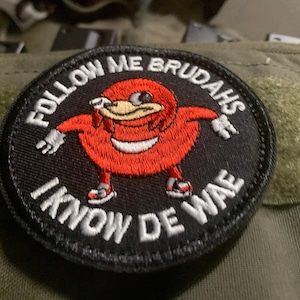 Puede incluir: Un parche bordado en blanco y negro con un personaje de dibujos animados rojo en el centro. El texto alrededor del personaje dice "Follow Me Brudahs I Know De WaE".