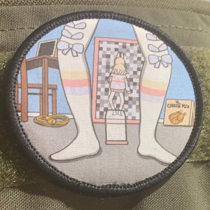May include: A round, black and white patch with a cartoon image of a person with long legs wearing white socks with pink and blue stripes and bows. The person is standing in front of a checkered pattern and a box that says "The Chicken Pizza".