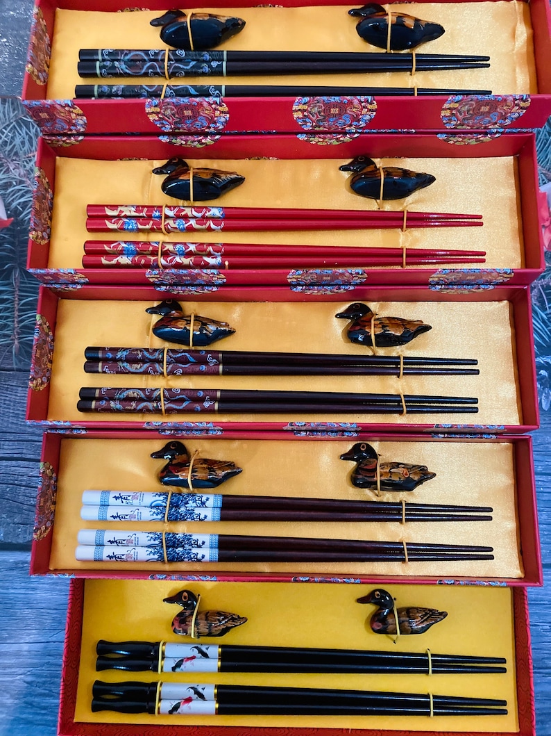 May include: Five sets of chopsticks in red and black boxes with duck-shaped handles. Each set includes two chopsticks with a decorative design. The boxes have a gold background with Chinese characters.