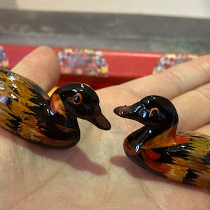 May include: Two small wooden duck figurines with black, brown, and orange paint. The ducks are facing different directions and have detailed features.