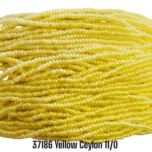 May include: A collection of small, round, yellow Ceylon glass seed beads arranged in multiple parallel strands. The beads have a smooth, glossy finish and a uniform size. The text 37186 Yellow Ceylon 11/0 is printed in black at the bottom.