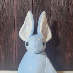May include: A light blue plush bat with white ears. The bat is a soft, cuddly toy with a sweet expression.