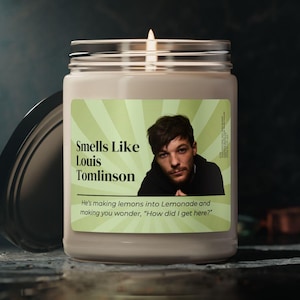 Puede incluir: Una vela blanca encendida en un tarro de cristal con tapa plateada. La etiqueta presenta una foto de un hombre y el texto "Smells Like Louis Tomlinson". No se especifica el aroma de la vela. El fondo es oscuro.